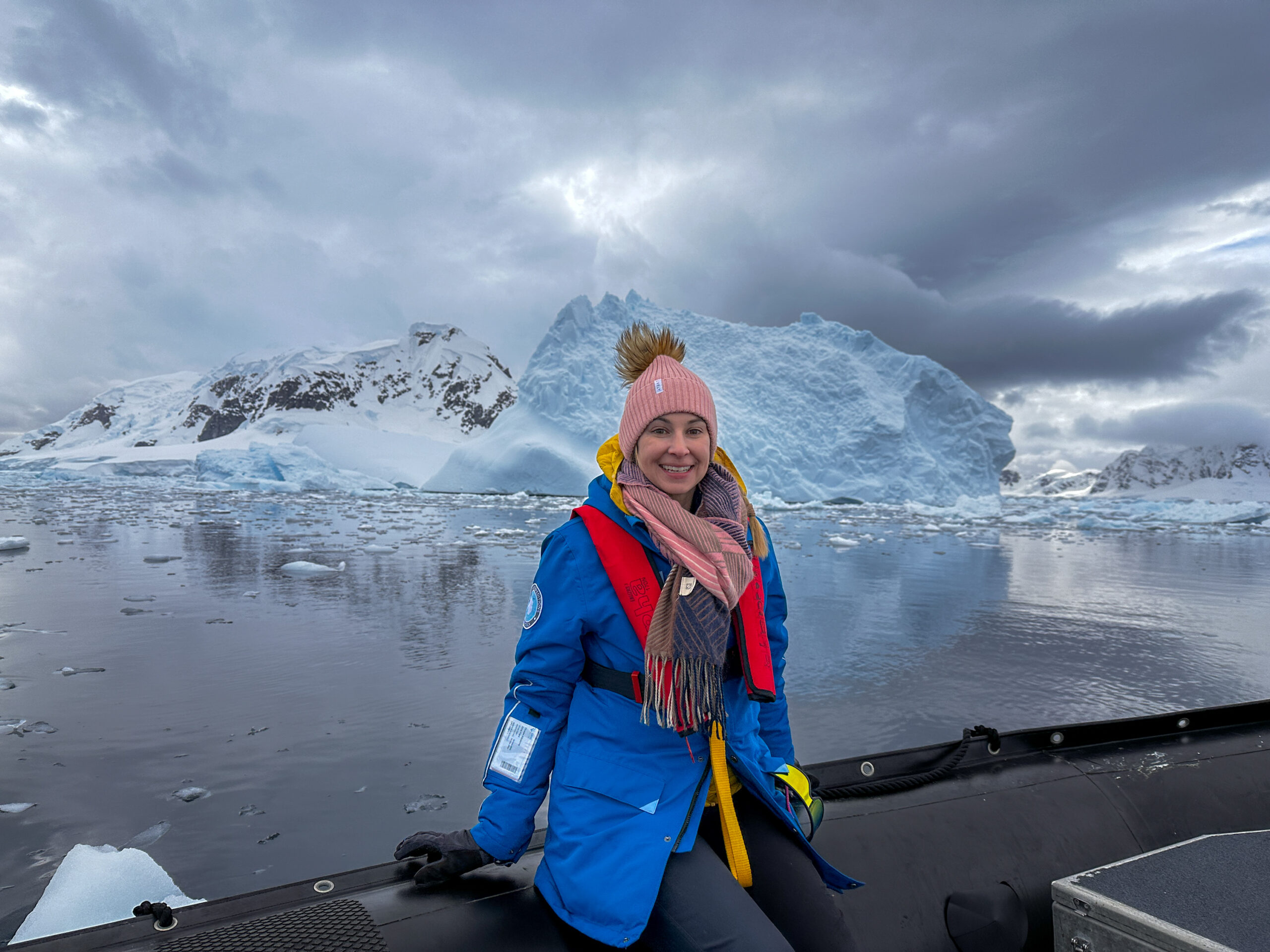 Woman in cold weather gear sitting on the edge of a zodiak in the sea