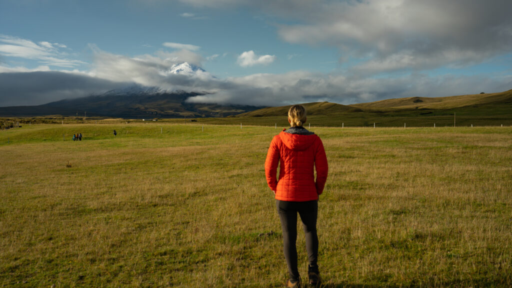 Women in red coat stands in front of the Cotopaxi volcano in Ecuador