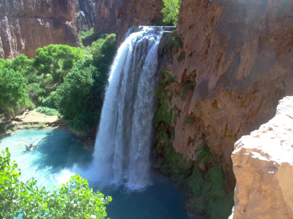 View of the turquoise waters and swimming hole below Havasu Falls during summer with greenery and rock formations around for a list of the best backcountry swimming holes to explore in summer