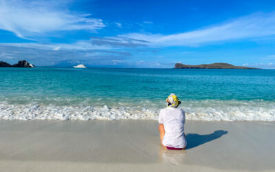 woman sits on a white sand beach in the Galapagos