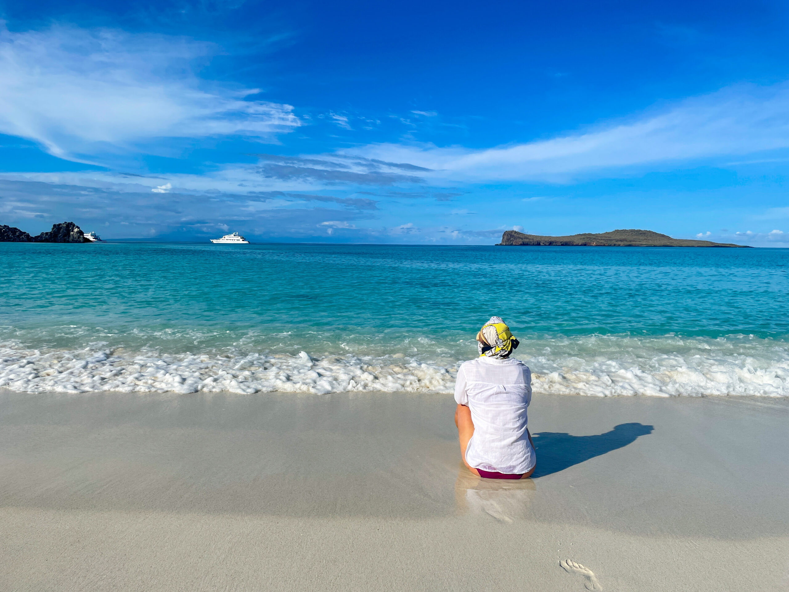 woman sits on a white sand beach in the Galapagos