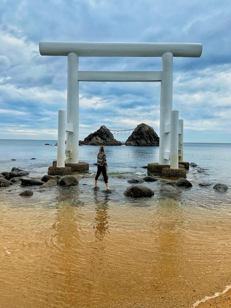 Alice Ford stands in front of Sakurai Shrine in Itoshima, Fukuoka featuring white arch torii gates over the sea during a solo travel Japan experience 