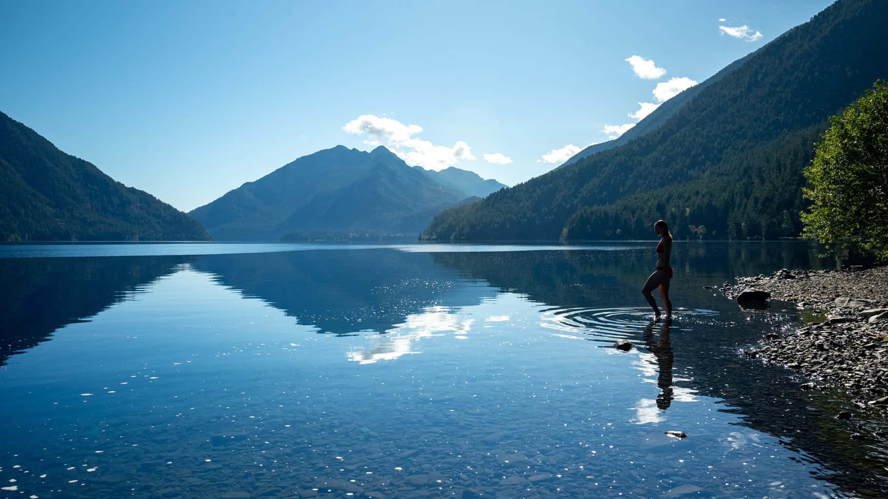 Shot of Lake Crescent with the Olympic Mountains reflecting on the water's still surface as Alice Ford stands ready to take a morning swim on a beautiful day during her 4-day itinerary for Olympic National Park