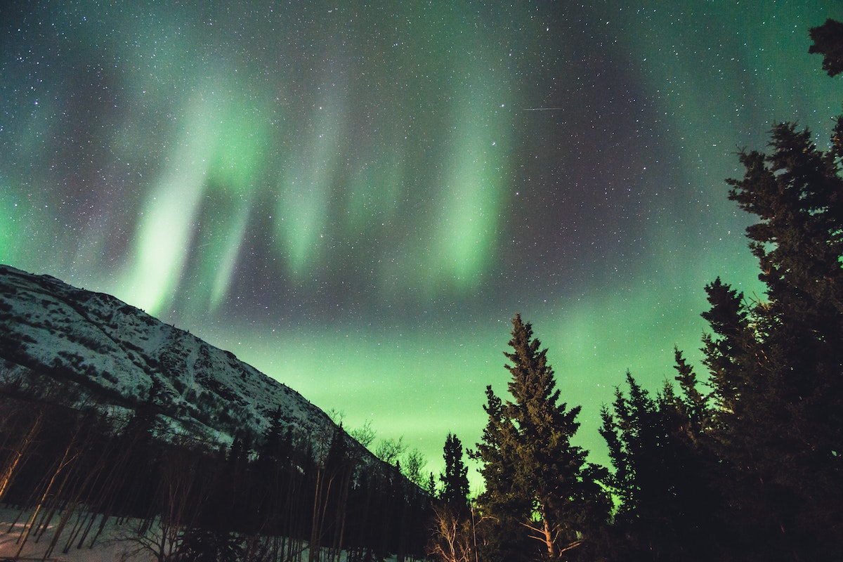 Green northern lights light up the night sky above a snow covered hill
