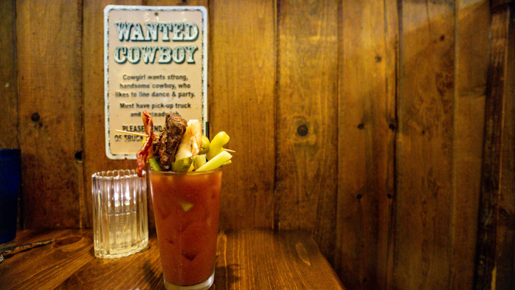 bloody mary with multiple toppings and sign that reads Wanted Cowboy