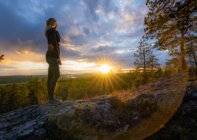 Woman standing on a mountain looking at the midnight sun