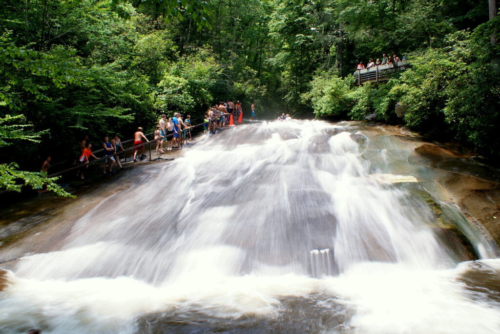 Water running over Sliding Rock in Pisgah National Forest, NC as swimmers line up on the side to enjoy the natural water slide at one of the best backcountry swimming holes in the U.S.