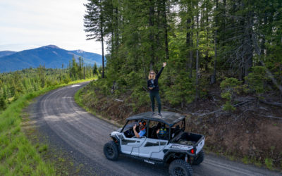Woman standing on an atv in the forest with 2 people waving