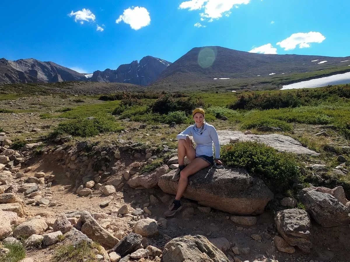Alice resting on a boulder in an alpine meadow beneath mountains