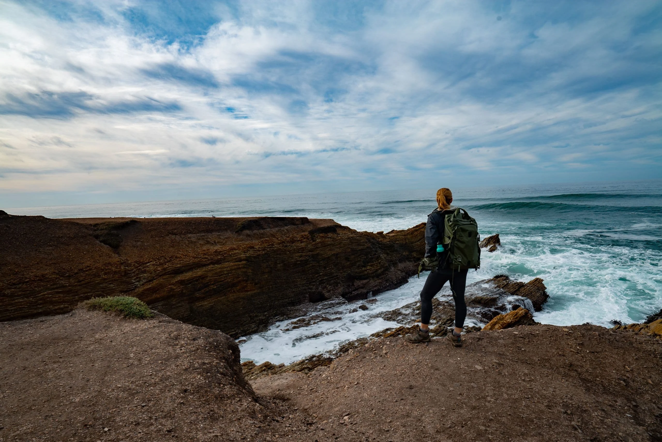Alice standing on dark sea rocks above crashing surf