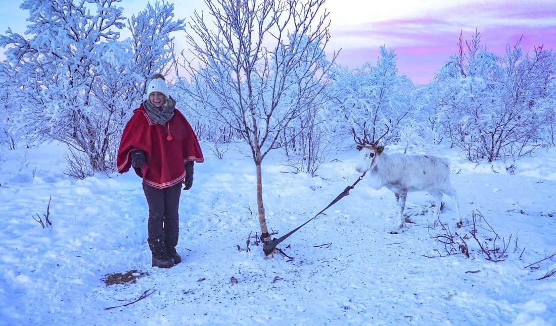 Alice walking through deep snow in a red Sámi coat