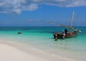 A wooden dhow anchored in clear turquoise water off a white-sand beach in Zanzibar