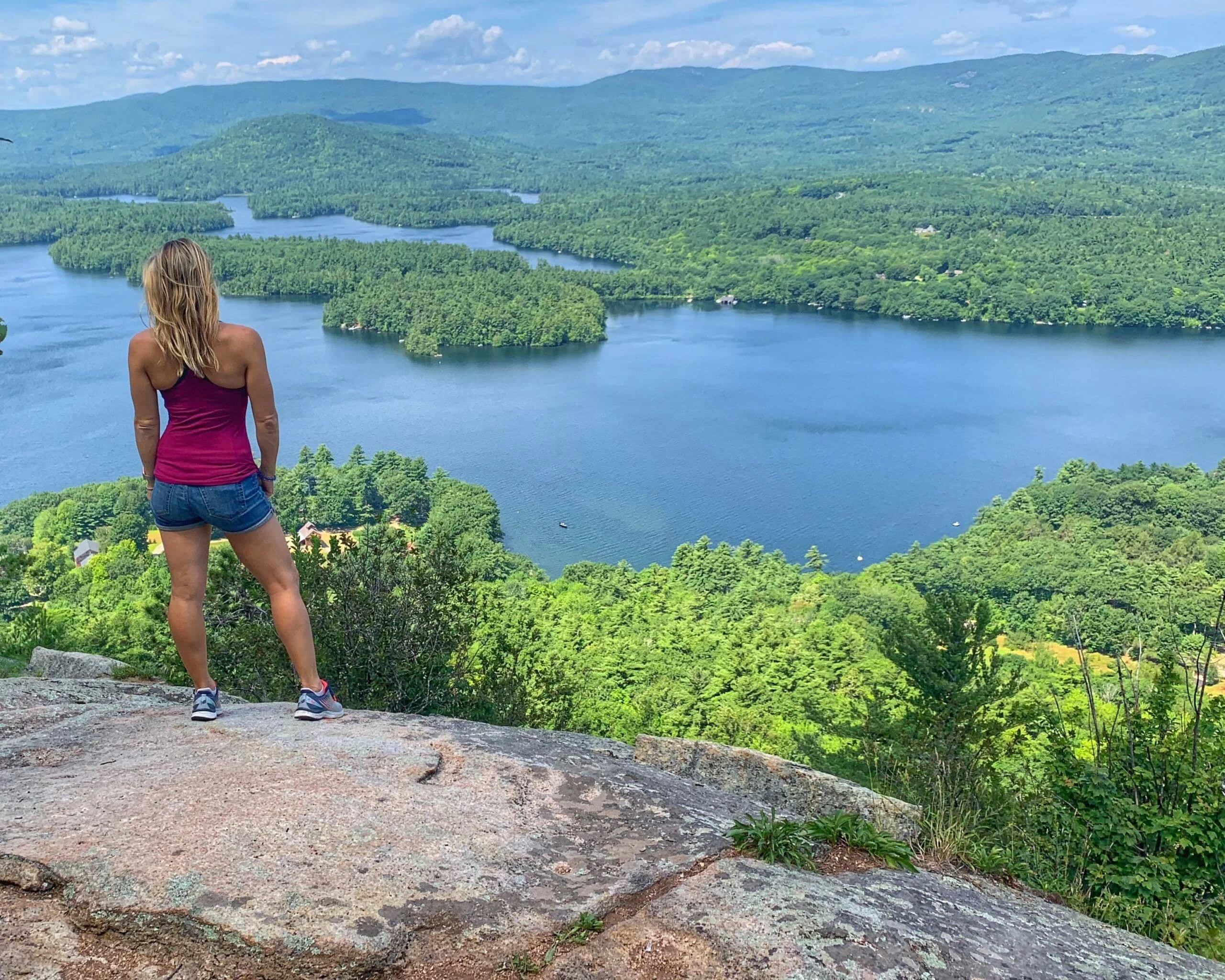 Alice stands on a granite outcrop above a forested lake, looking out
