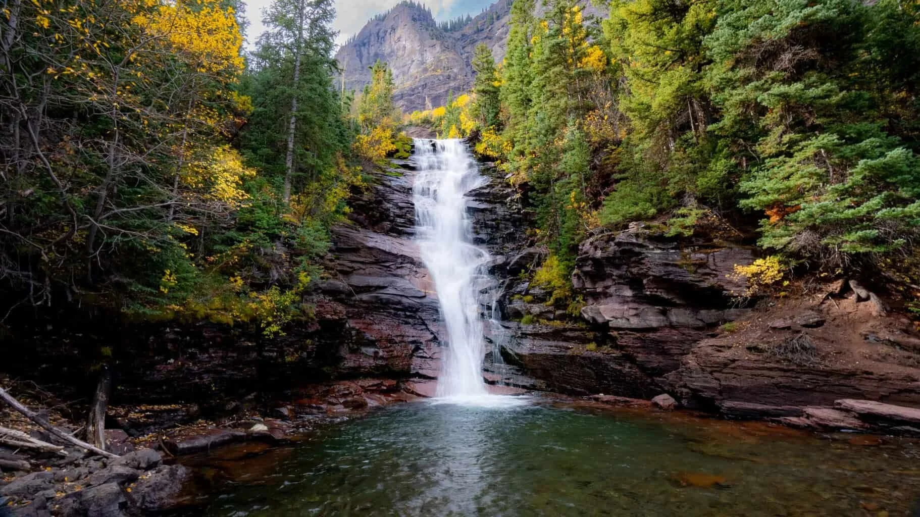 A waterfall pouring into a forest pool between red rock walls