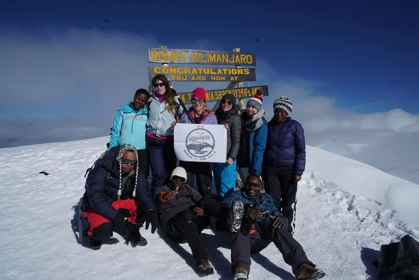 A climbing team celebrating at the snowy summit sign of Mount Kilimanjaro