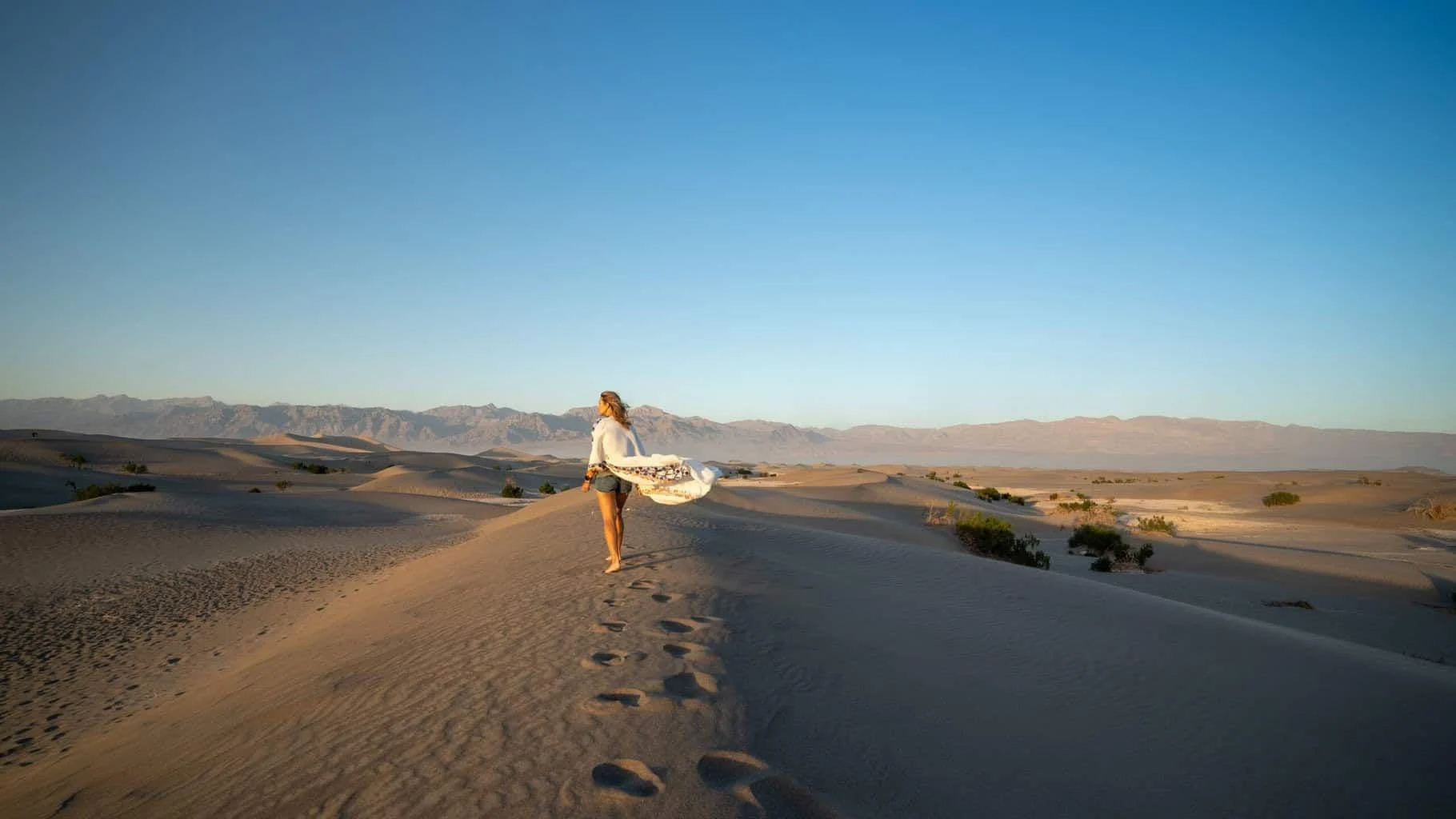 A traveler walking along a ridge of sand dunes at golden hour