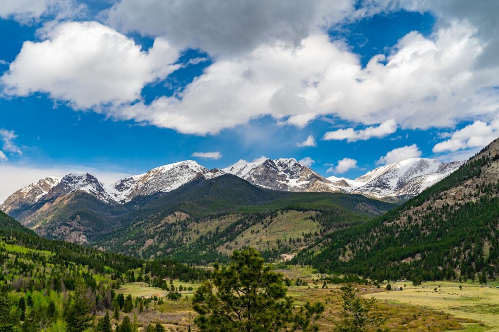 Wide view of Rocky Mountain National Park with peaks, clouds, and greenery in view on a beautiful day for a 14-day road trip across the U.S.